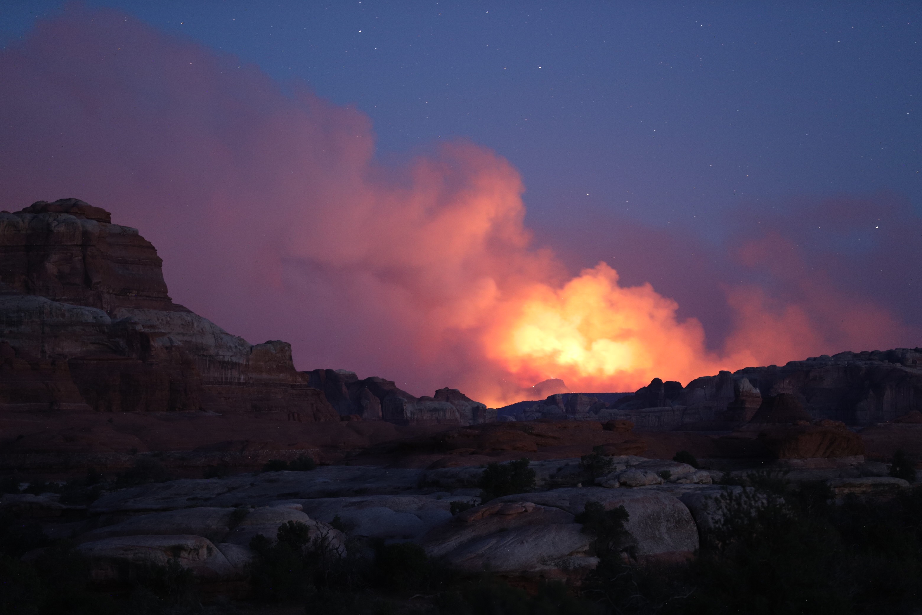 Smoke clouds rise above sandstone rocks at twilight