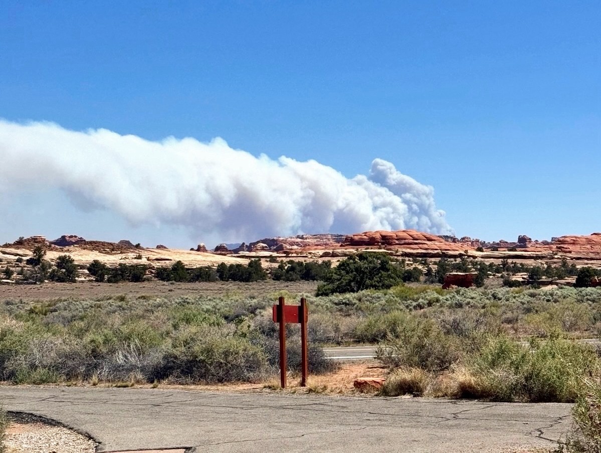 smoke plume visible above desert landscape; paved road and sign in foreground