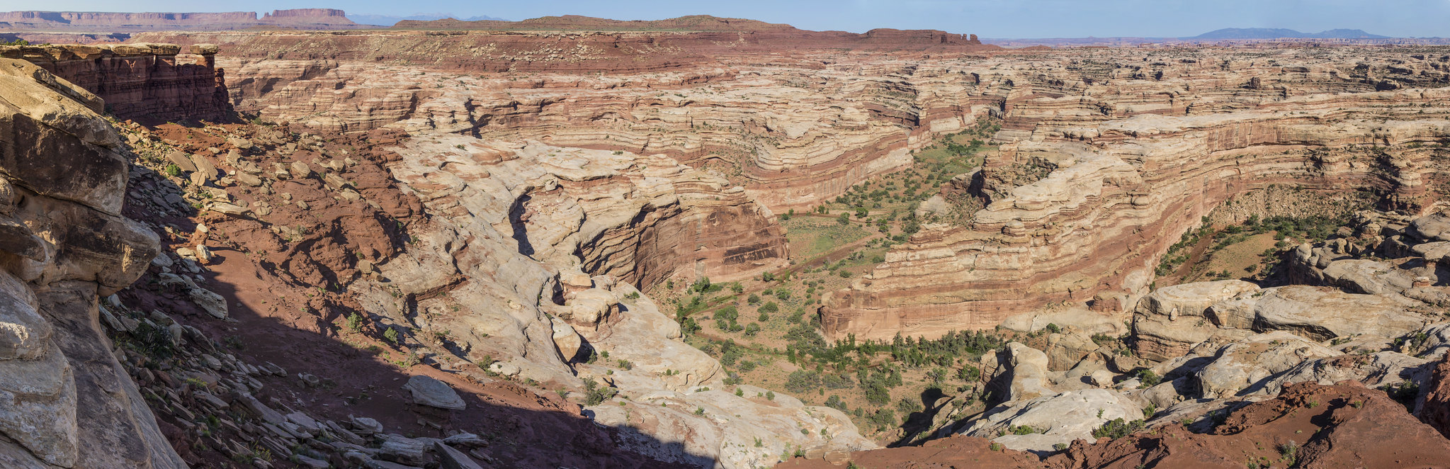 Swirls of tan and reddish-brown sandstone swirl in a maze of connected desert canyons under a blue sky.