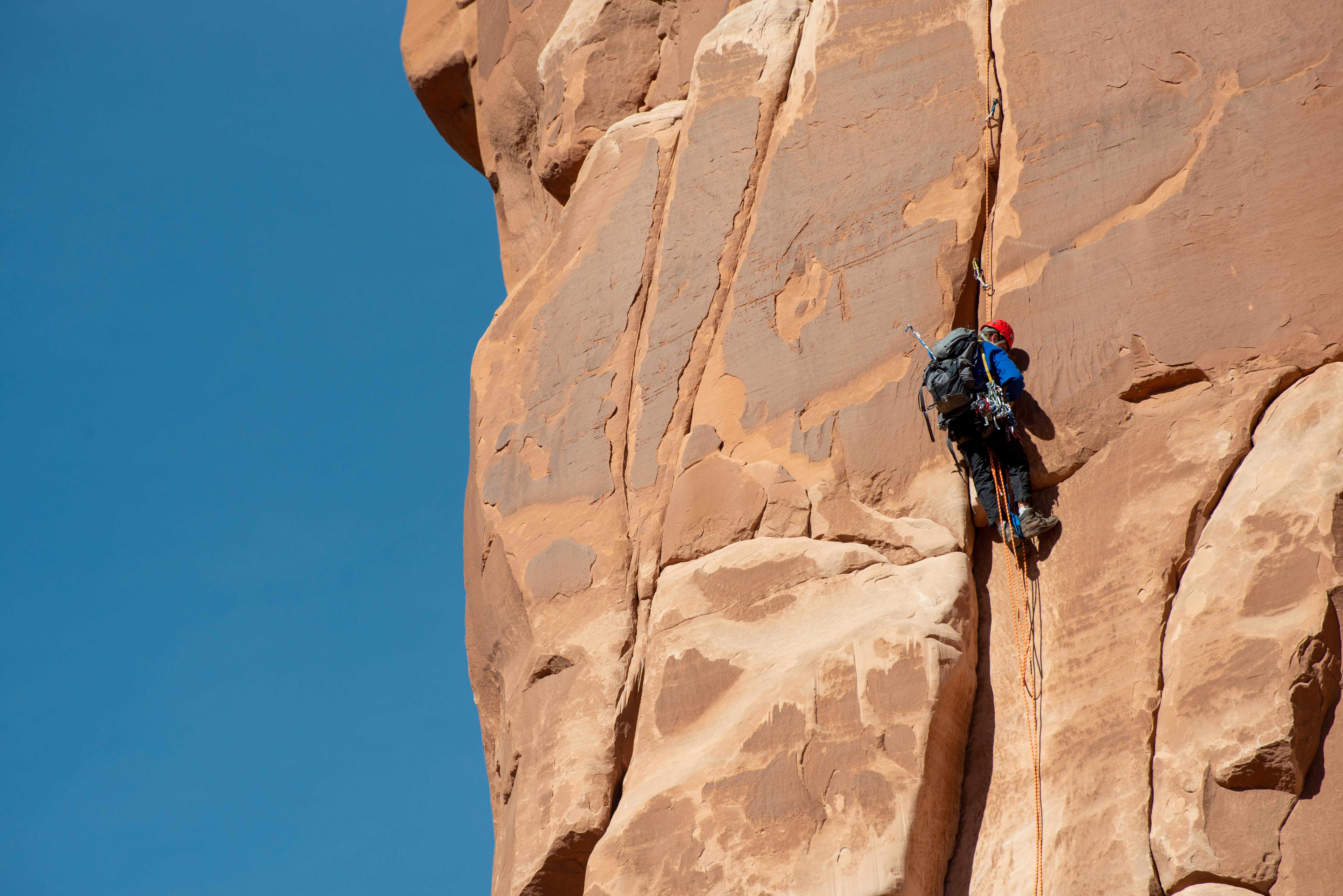 Climber with a helmet, backpack and other climbing gear ascends a route on a sandstone wall