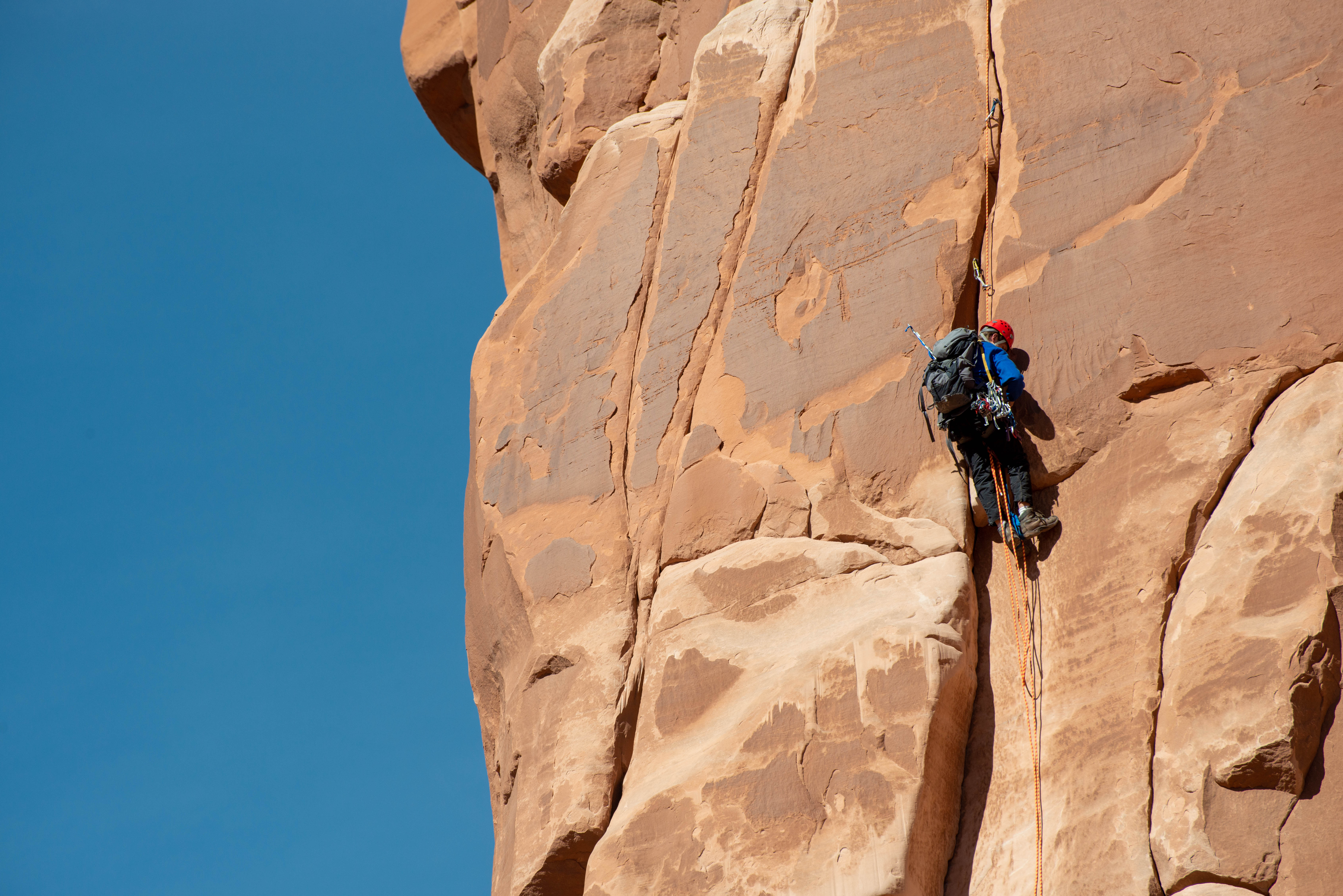 A climber ascends a complex route. Climber with a helmet, backpack and other climbing gear ascends a route on a sandstone wall