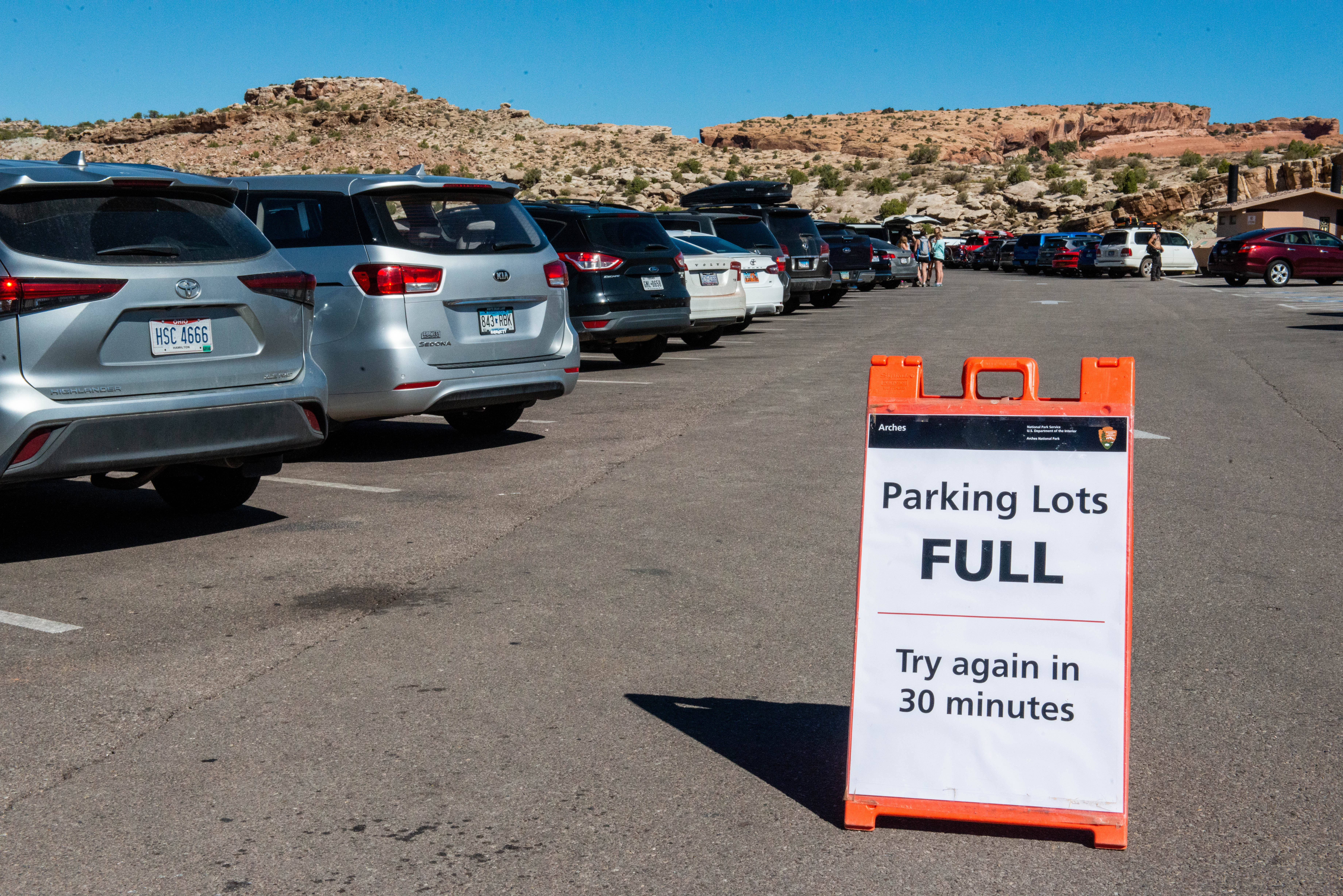 sign saying "parking lots full; try again in 30 minutes" next to row of parked cars
