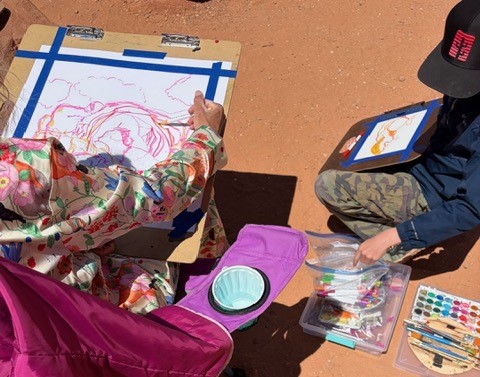 adult and child draw a stone arch on paper with brightly colored markers, red dirt in background