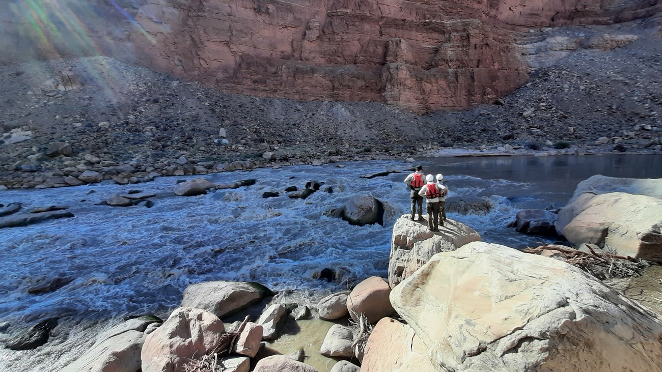 Three people look out over rapids