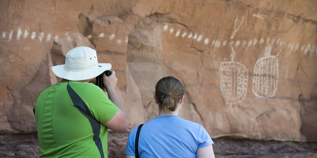 Two people looking at pictographs on a rock wall