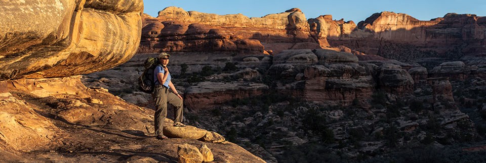 A hiker stands on a cliff edge with canyons in the background A hiker stands on a cliff edge with canyons in the background