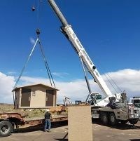 crane lifts small brown building into blue sky