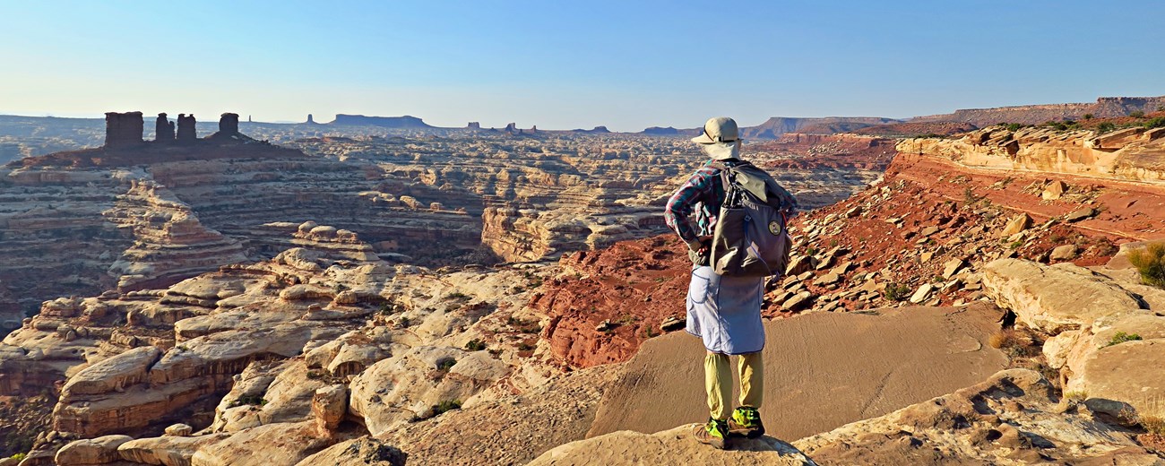 Person with backpack standing at an overlook above canyons