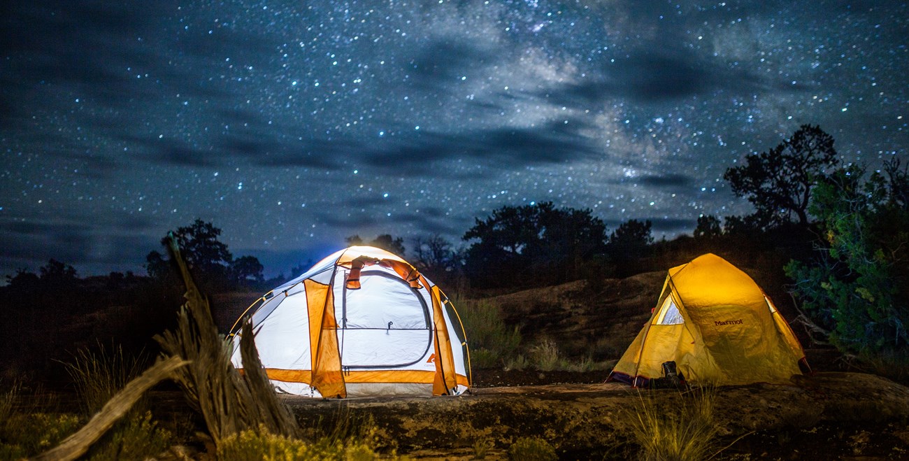 Two tents are illuminated under the night sky in the backcountry of Canyonlands