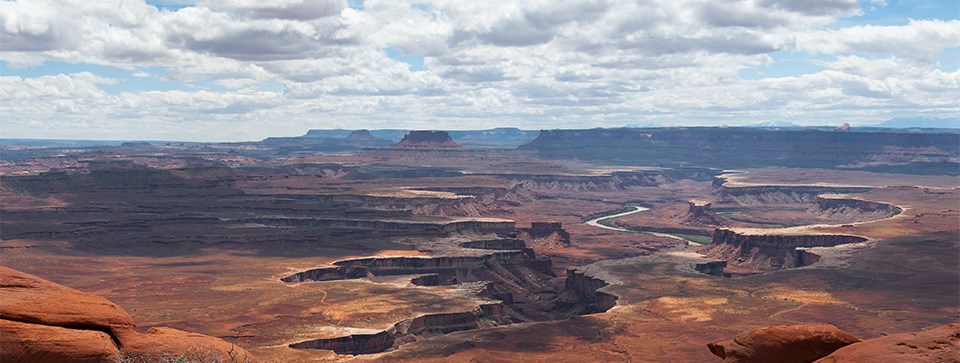 a vast view a river at the bottom of red canyons and white clouds overhead