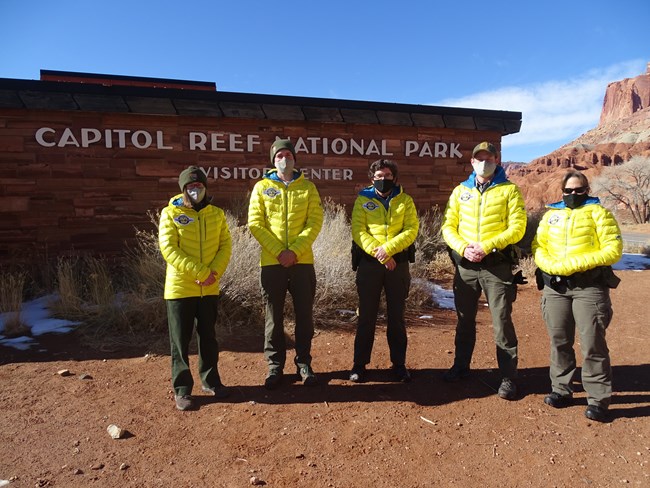 Five people wearing bright yellow jackets, standing outside a stone building that reads "Capitol Reef National Park"