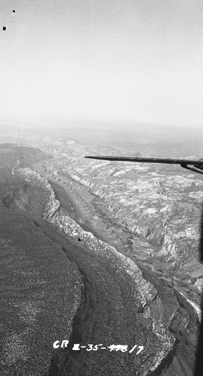 Black and white aerial photo of the Waterpocket Fold, a large monocline. A bit of a plane wing is in the middle of the photo