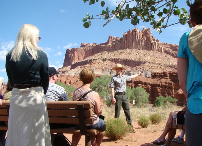 a ranger presenting a program to visitors with sandstone cliffs as a backdrop