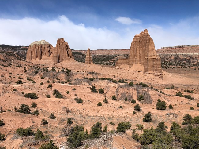 Tall, narrow monoliths of sedimentary rock rising from the ground, with blue sky and clouds in the background.