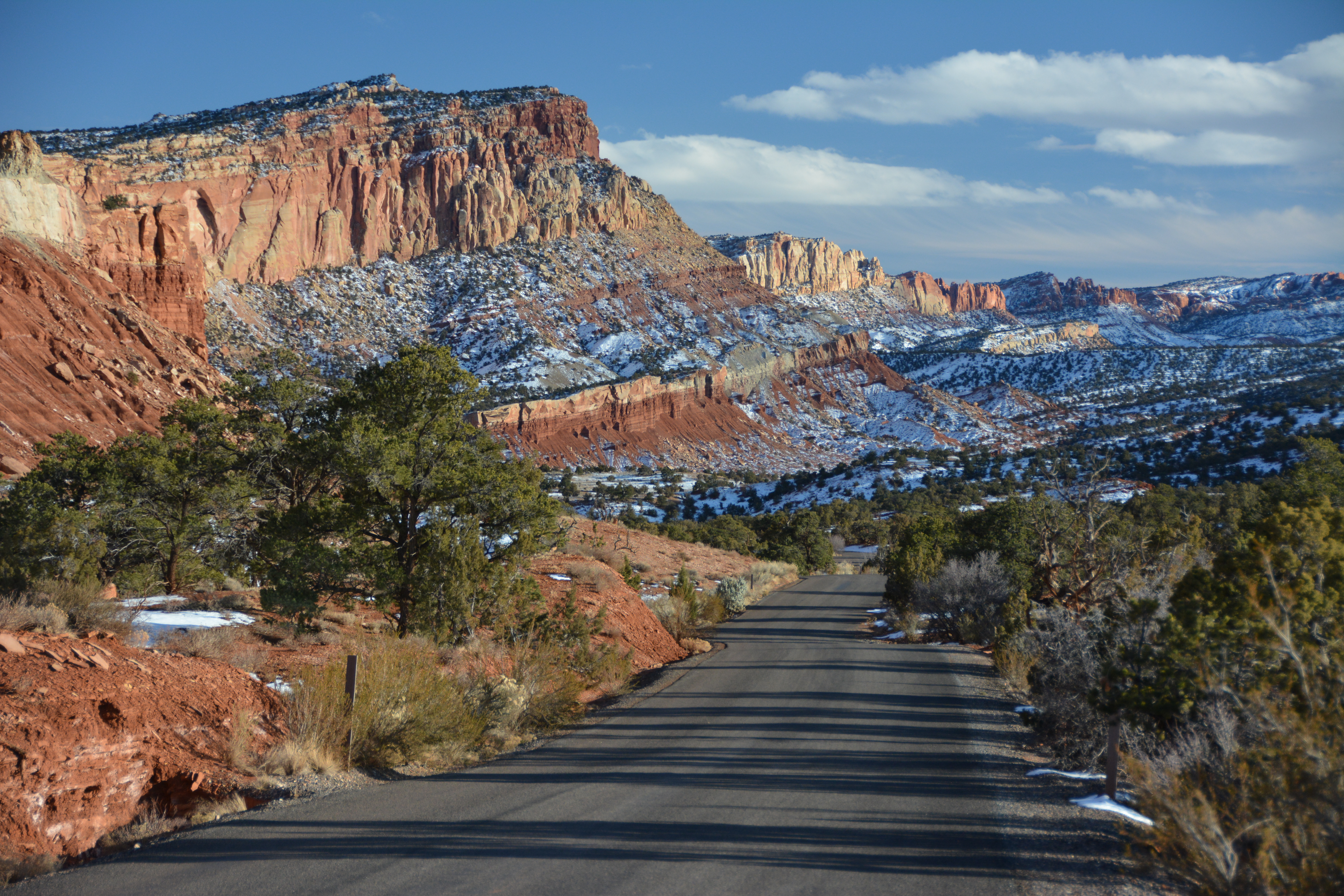 A road through red rock desert with a dusting of snow on the sandstone cliffs to the left side