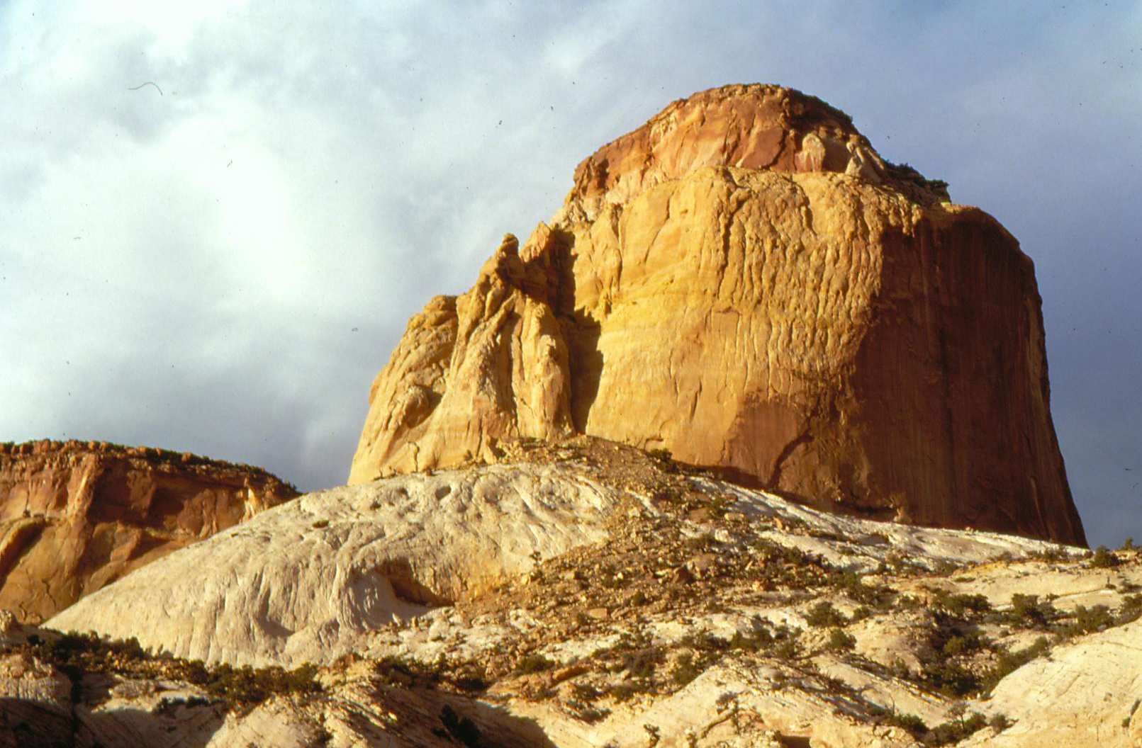 a golden tan colored sandstone monolith against a cloudy sky