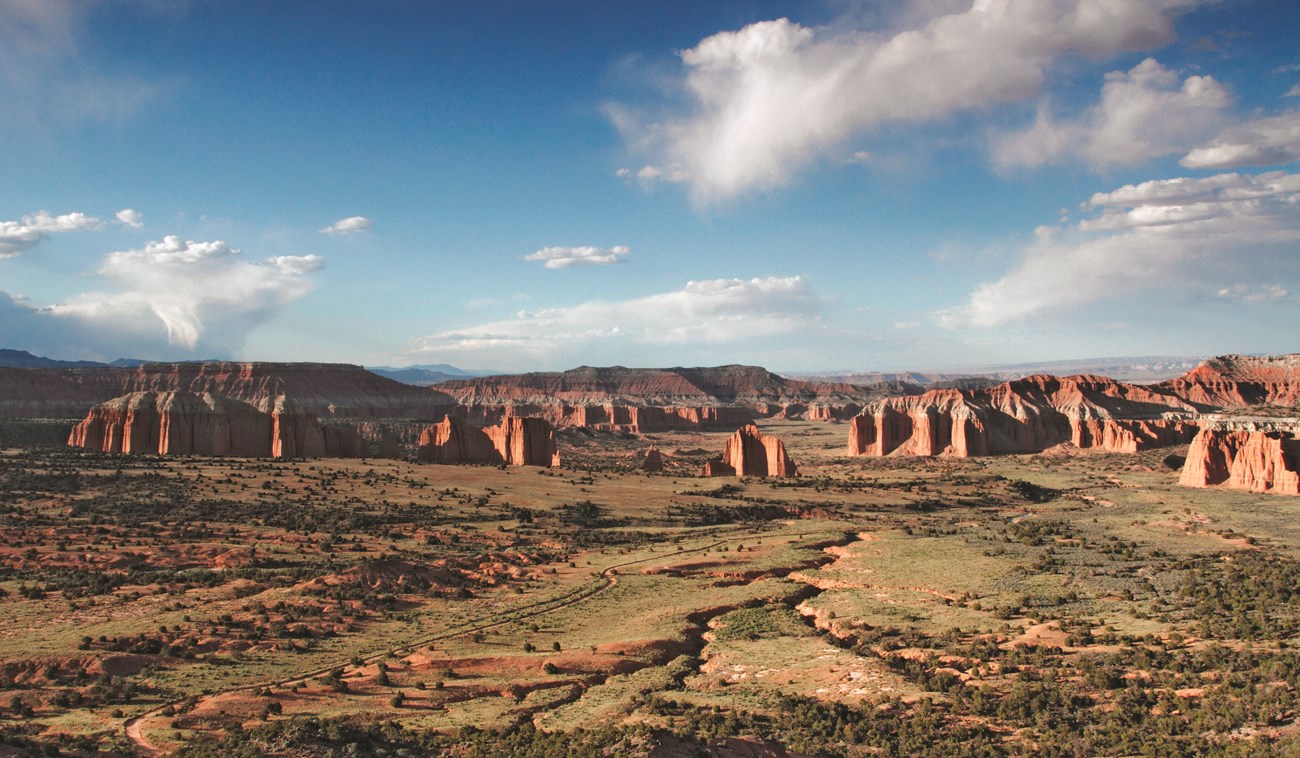 View from above looking down on grassy valley, with large reddish orange rock monoliths protruding out, and blue sky above.