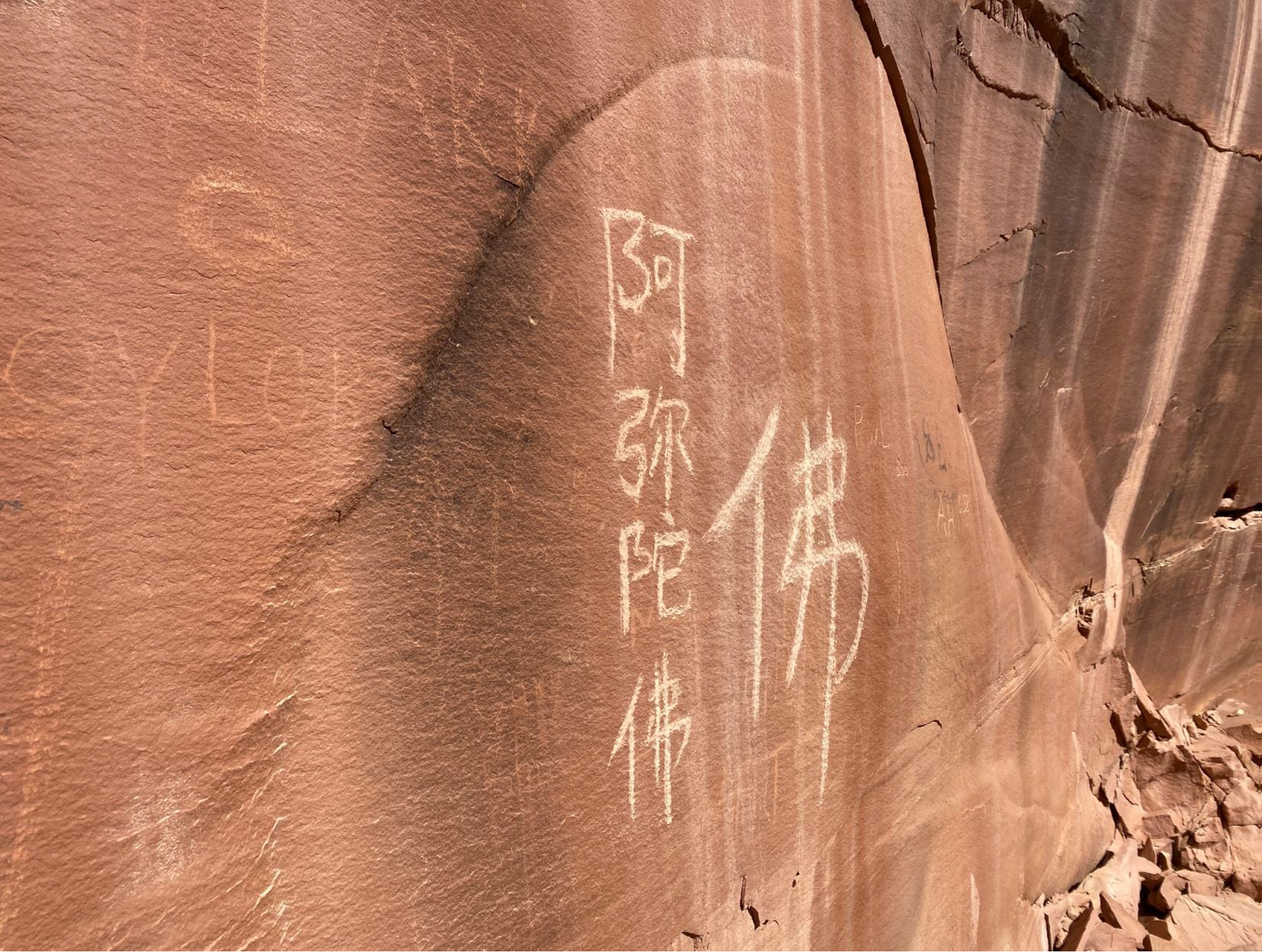 Characters carved into a rock wall stand out brightly next to historic inscriptions