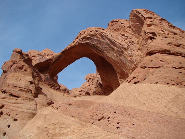 Oval-shaped arch in reddish orange sandstone, with blue sky behind and above.