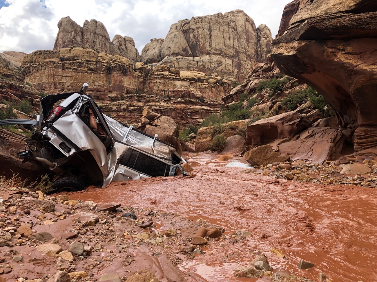 A silver vehicle half buried in a muddy streambed.