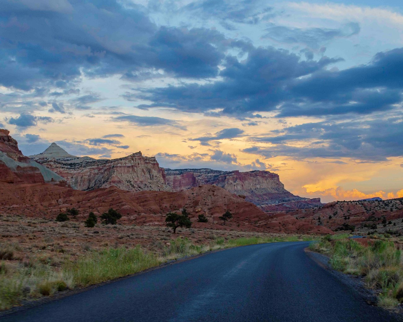 A paved road against a landscape of red cliffs and a cloudy sky.