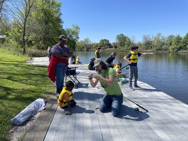 On a dock, fishing children and a man rethreading pole