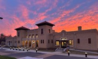 A yellow brick building with twin towers at sunset.