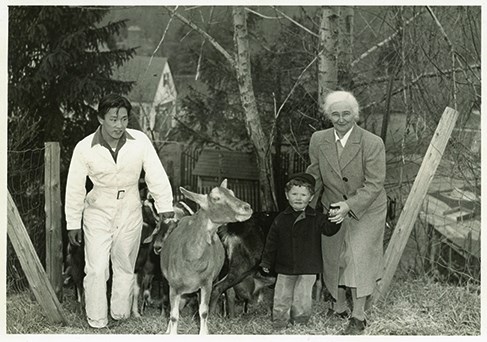 Black and white image of a man holding a goat next to a woman with a small child