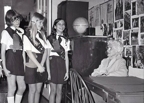 image of an older woman sitting in a chair next to 3 girl scouts in uniform