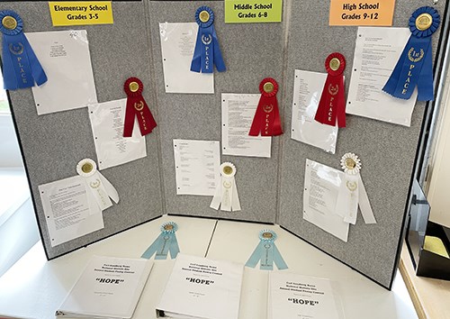 A gray display board has printed poems and award ribbons.