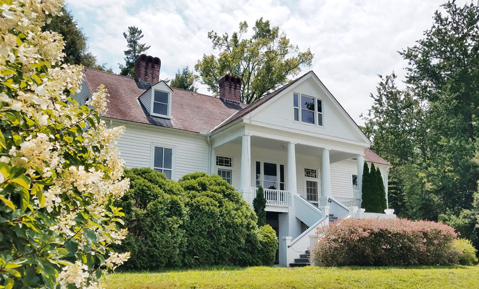 Sandburg Home as viewed in late summer surrounded by green trees, with white blooms from a hydrangea in the foreground