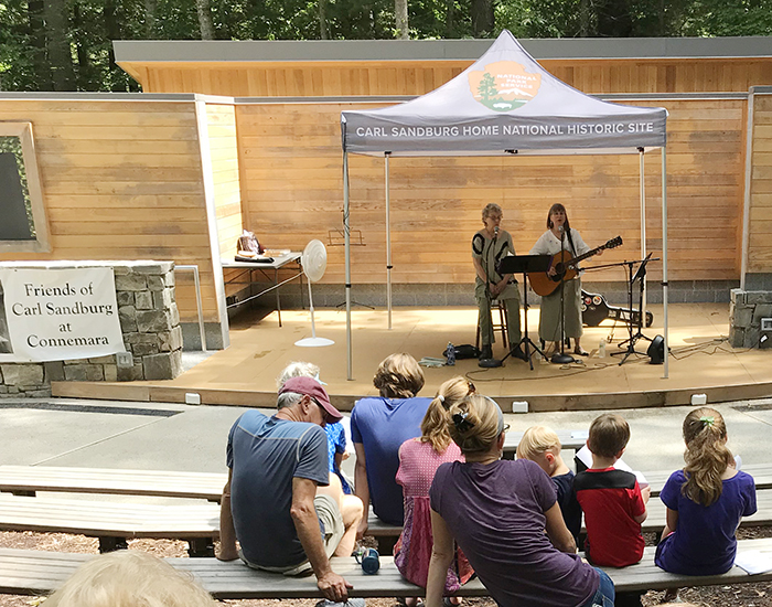 A stage with 2 performers and 8 people sitting in the audience on benches