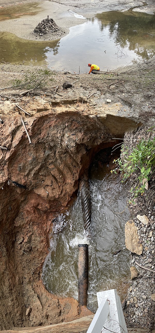 View of a large hole in a lakebed near a dam with a broken pipe in the bottom.