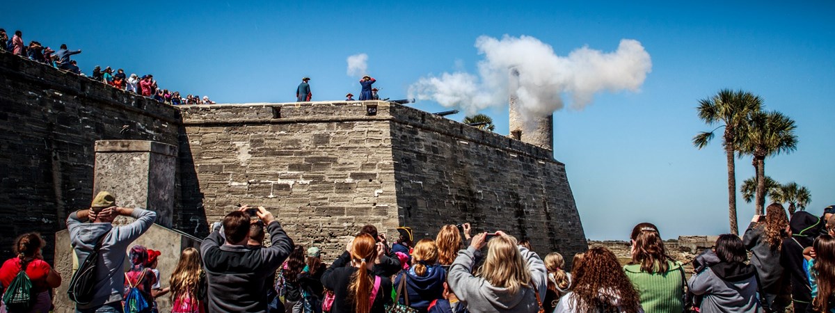 Cannon firing with smoke coming out of barrel. View from water battery, eastern moat, with a crowd of people watching the cannon fire.