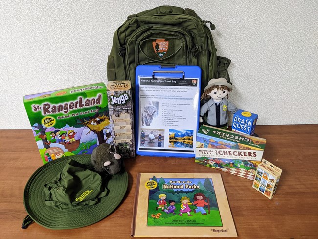 A green backpack with books, toys, and more on the topic of the National Park Service.