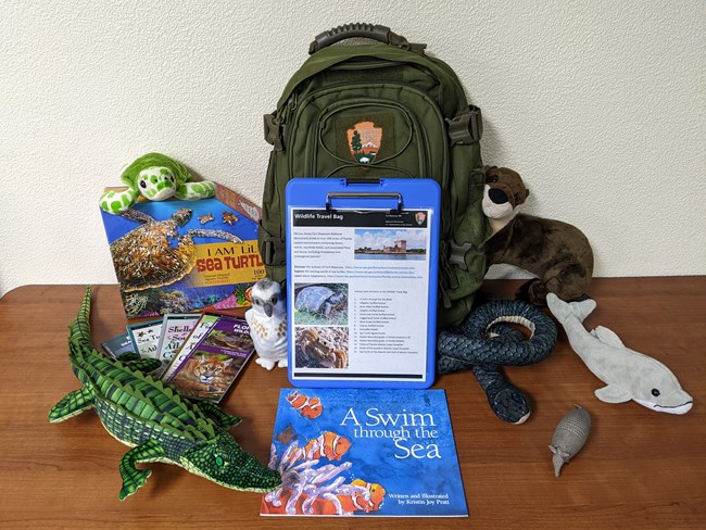 A backpack with stuffed animals and a book on wildlife.