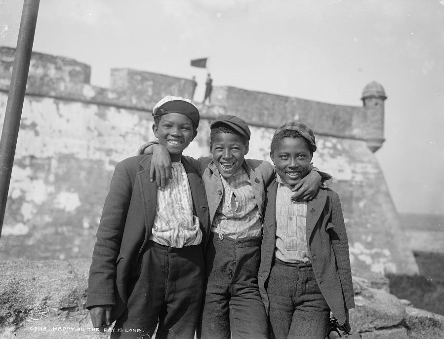 Black and white photograph of three African American boys smiling in front of the fort.