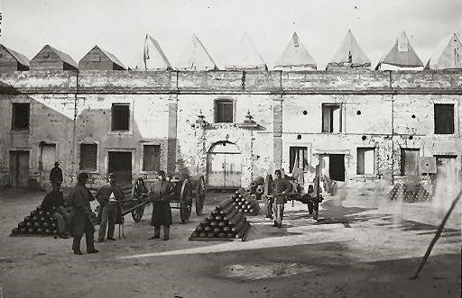 Soldiers stand in the courtyard amidst large pyramids of cannonballs.