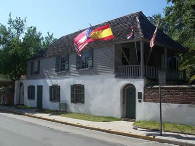 Modern photograph of the Gonzalez-Alvarez House with flags of the different nations that controlled St. Augustine out front.