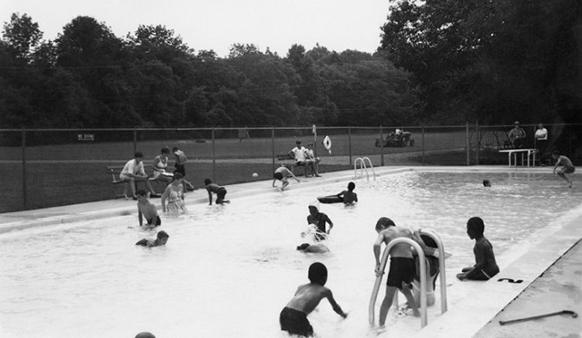 The Camp Greentop pool in the 1970s. Children can be seen descending into and playing in the pool. In the background, there are sports fields.