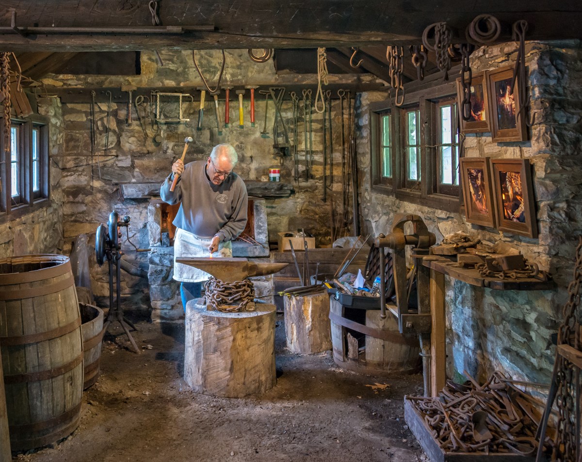 Blacksmith working iron over anvil in blacksmith shop