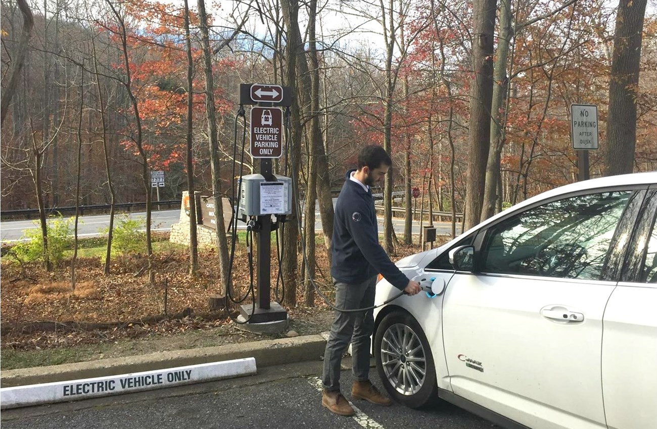 A man plugs in an electric car at a charging station in a parking lot at Catoctin Mountain Park.