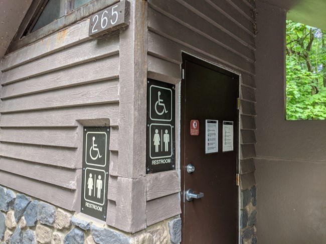 Side of Outdoor Restroom Building. The building has multiple universal signs indicating it is a restroom and wheelchair accessible.