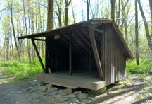 Wooden, 3-sided shelter with roof, located in the woods. Wooden, 3-sided shelter with roof, located in the woods.