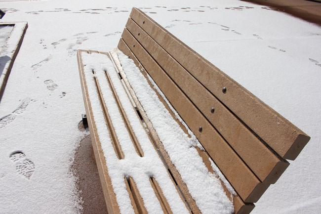 A park bench sits atop a concrete surface covered in snow.