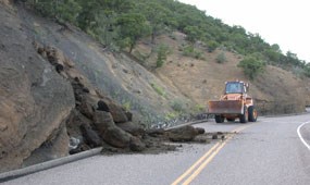 color photograph of front end loader clearing rock slide on road