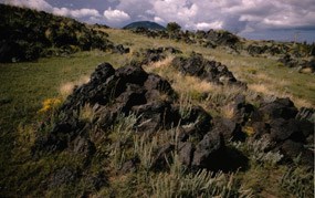 color photograph with lava flow close up foreground and tip of Capulin Volcano in far background