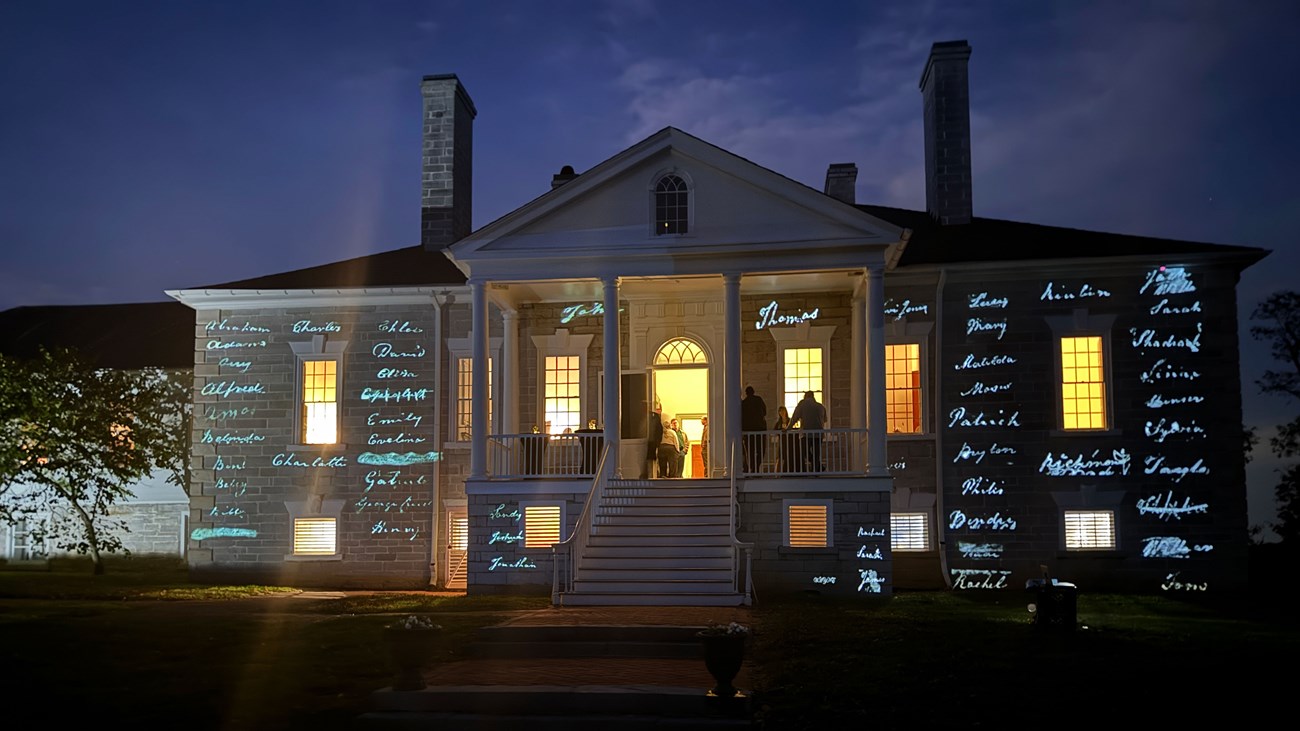 Names of enslaved persons are project onto the wall of antebellum plantation house at night.