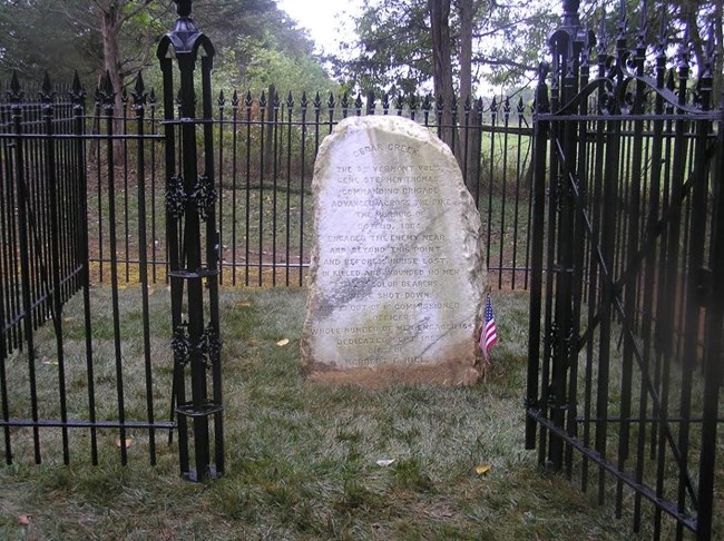 A metal gate encloses a marble monument with inscriptions honoring an army regiment.