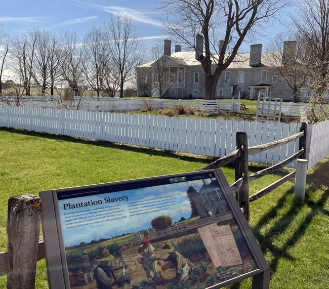 An outdoor exhibit panel at an antebellum manor interprets plantation slavery.